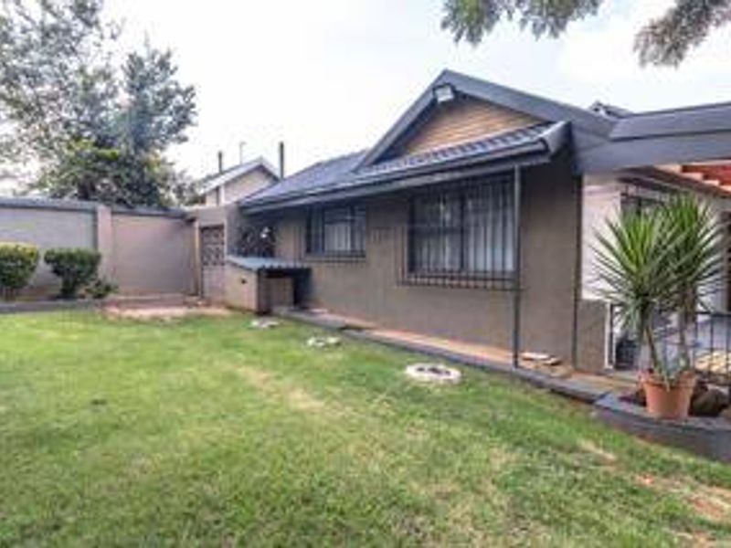 A view of the rear exterior of the house featuring a lawn, perimeter wall, and a covered patio area with security bars on windows.