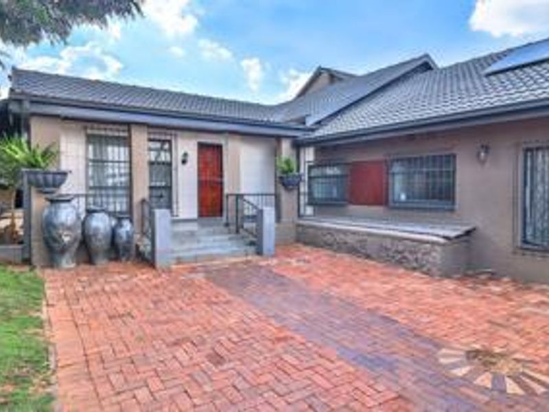 Front entrance area featuring a brick paved driveway, stone masonry accents, and secure window treatments under a tiled roof with solar panels.