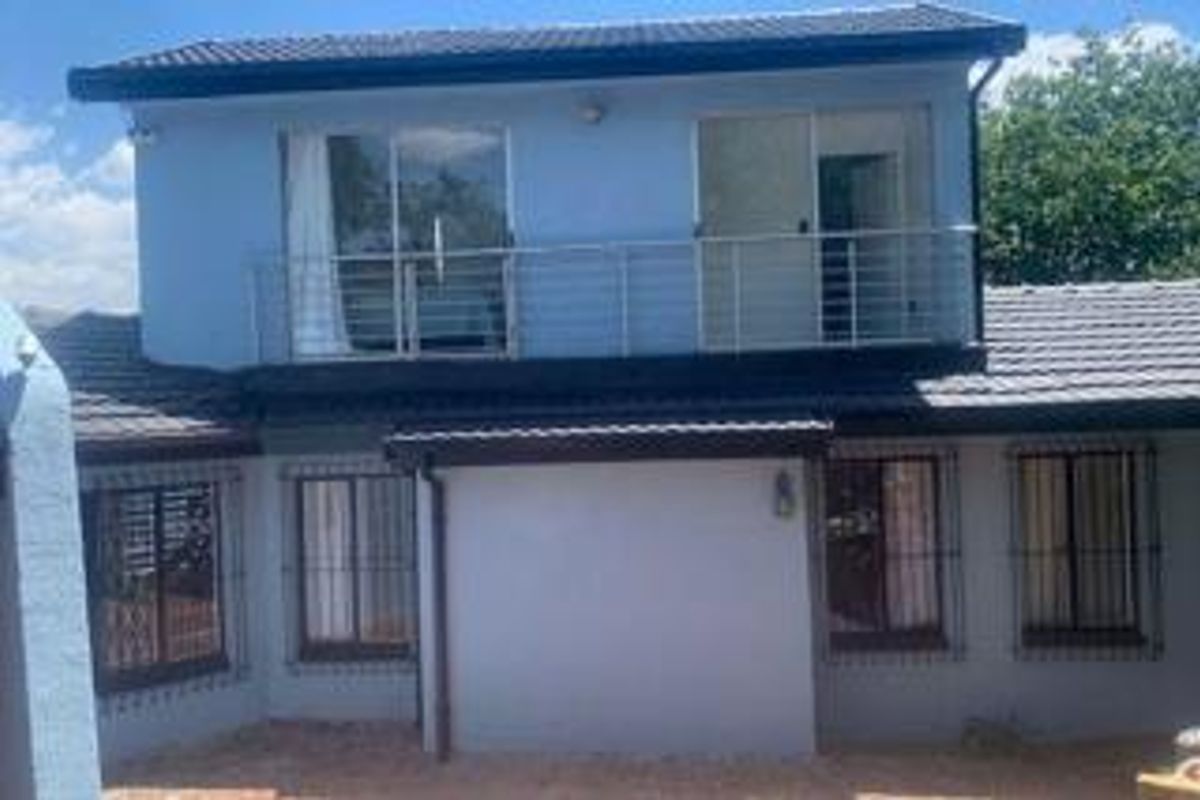 Rear elevation of a two-story house featuring a balcony with metal railings, sliding glass doors, and security bars on the ground floor windows.