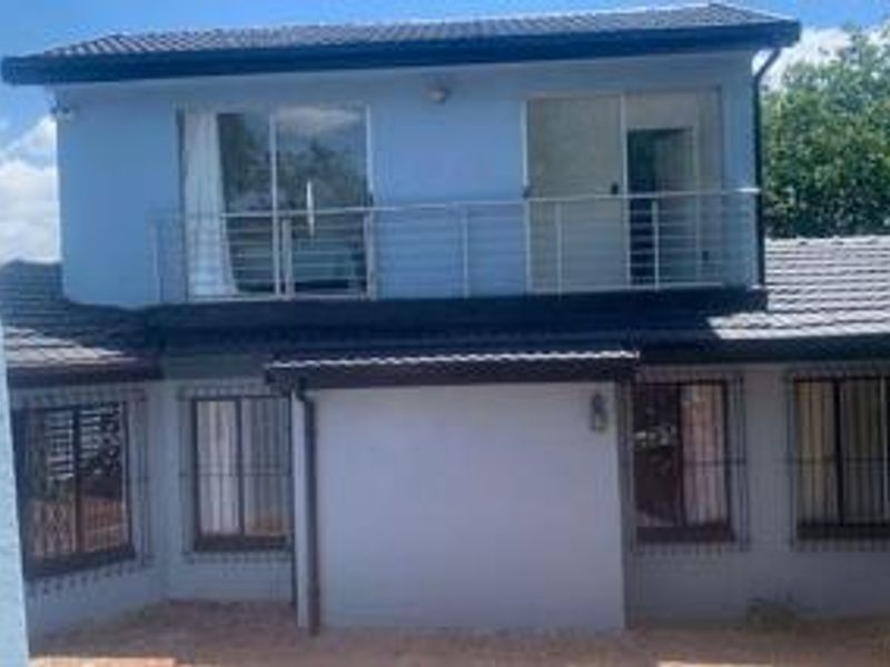 Rear elevation of a two-story house featuring a balcony with metal railings, sliding glass doors, and security bars on the ground floor windows.