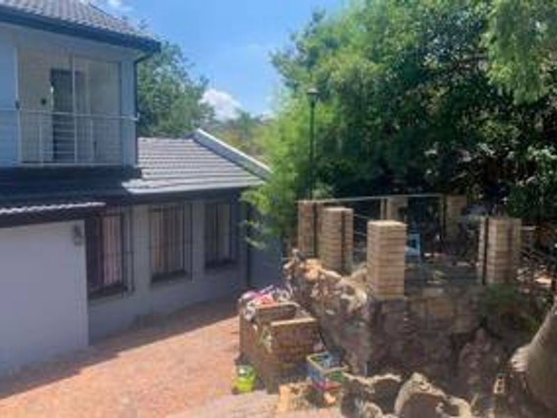 Rear view of the property featuring a multi-level outdoor area with a balcony, brick pillars, and stone retaining walls.