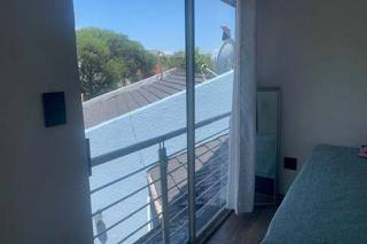 Bedroom featuring laminate flooring and a sliding glass door leading to a small balcony with metal railings.