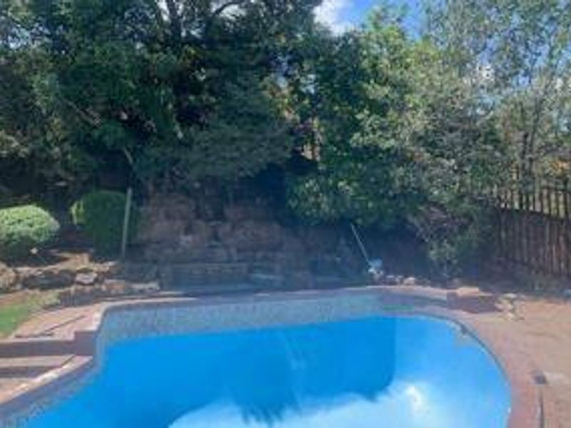 Outdoor pool area featuring a swimming pool, stone retaining wall, and perimeter fencing, set against a backdrop of mature trees.