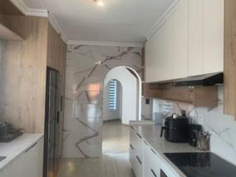 Modern kitchen featuring sleek built-in cabinetry, stone countertops, and elegant marble-look wall tiling, leading through an archway to the rest of the home.