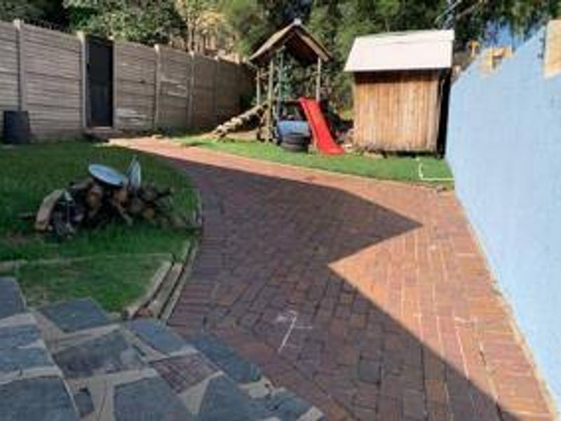 A rear garden area featuring a brick paved pathway, stone tiled patio, and perimeter boundary walls.