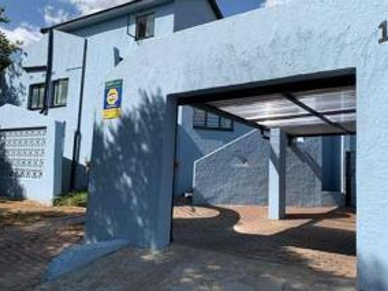 Front elevation of the property featuring a paved driveway, covered carport, and blue painted exterior walls with decorative breeze block detailing.