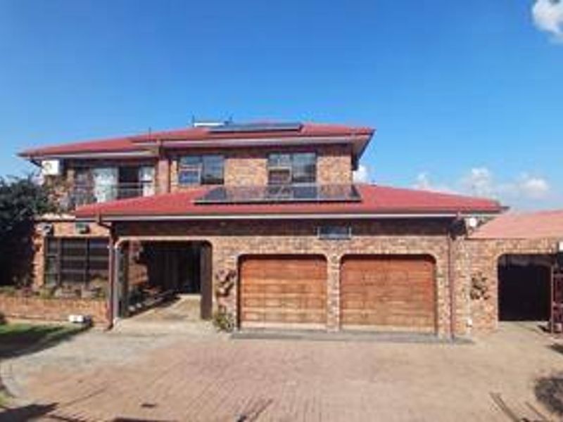 A double-storey face-brick house featuring a double garage, paved driveway, solar panels, and a balcony, presenting a well-maintained exterior facade.