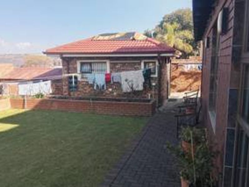 A rear view of the property featuring a brick exterior, tiled roof with solar panels, a paved walkway, and a well-maintained lawn area.