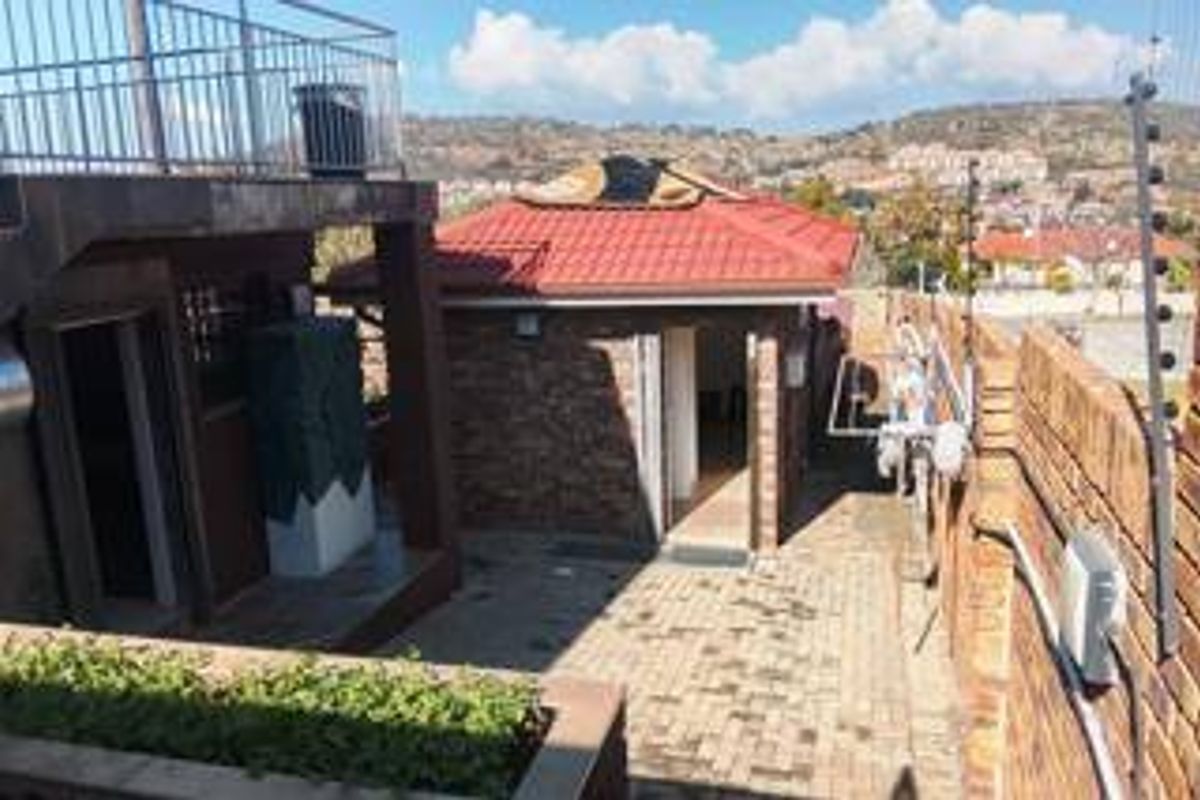 Rear exterior view featuring a brick structure with a tiled roof, paved courtyard area, and perimeter electric fencing.