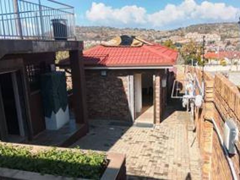 Rear exterior view featuring a brick structure with a tiled roof, paved courtyard area, and perimeter electric fencing.