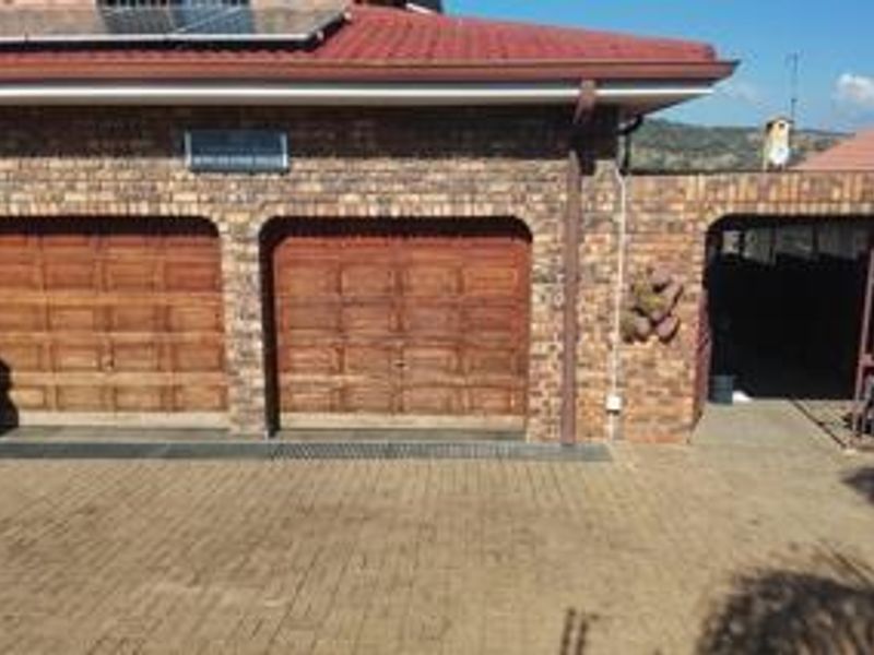 Exterior view of a double garage with wooden doors, brick facade, and paved driveway, featuring solar panels on the roof.