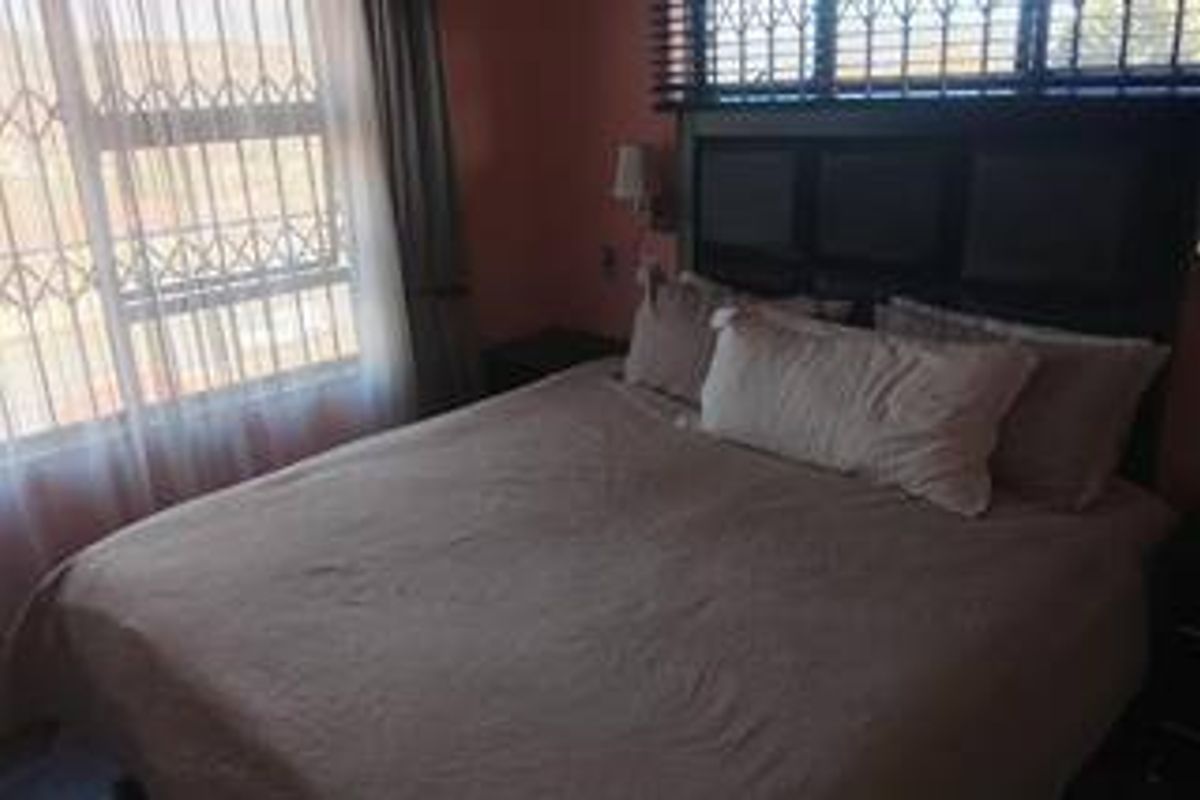 A bedroom featuring a built-in headboard, security bars on the windows, and wall-mounted lighting.