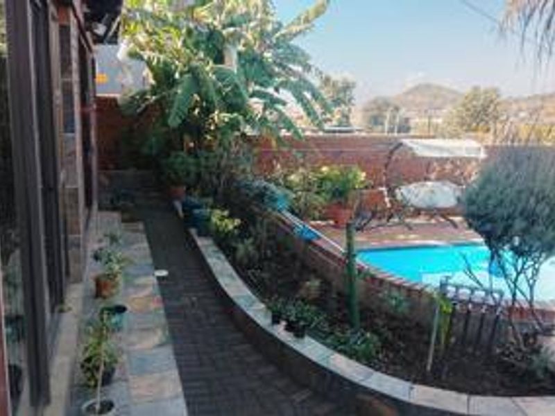 Outdoor pool area featuring a brick-paved walkway, raised garden beds, and a swimming pool with views of the surrounding landscape.