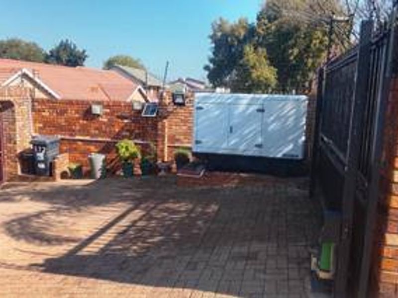 Front exterior area featuring a paved driveway, brick boundary wall, and a permanent generator installation.