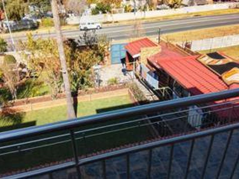 Elevated view from a balcony overlooking a residential garden, paved area, and adjacent street.