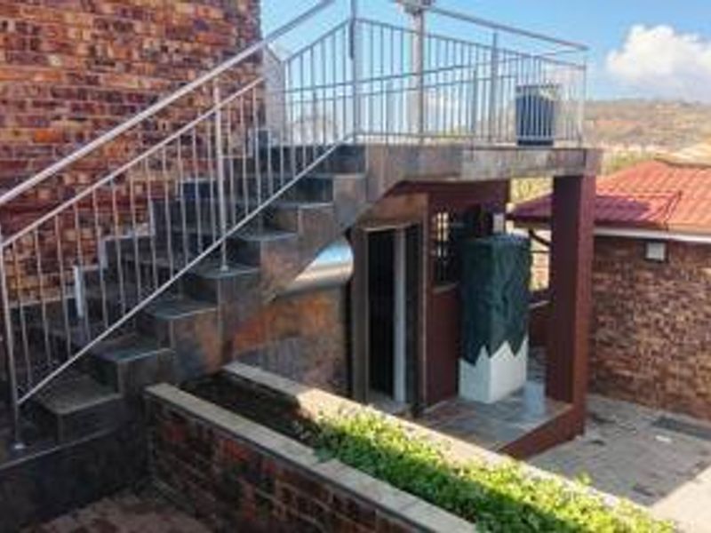 Exterior view of a rear property area featuring a tiled staircase with stainless steel balustrades leading to an elevated patio space.