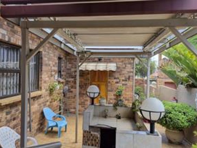 Covered outdoor patio area featuring a built-in braai, brick exterior walls, and security bars on windows, providing a functional space for outdoor entertaining.
