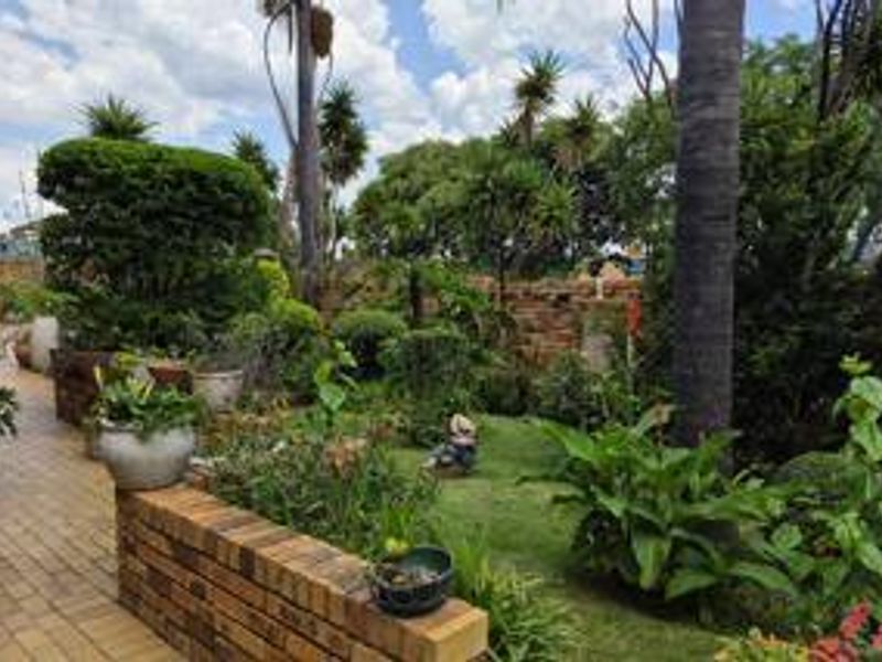 A well-established garden featuring a brick retaining wall, paved walkway, and mature trees, offering a lush and private outdoor space.