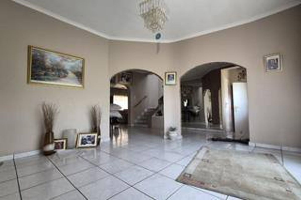 Spacious living area featuring tiled flooring, elegant arched doorways leading to a staircase, and a central chandelier, offering a bright and open layout.