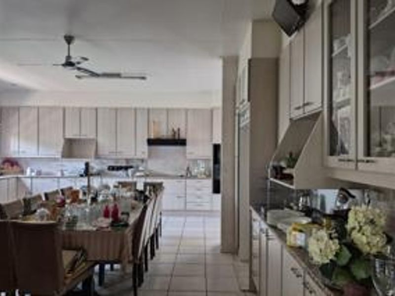 Spacious open-plan kitchen and dining area featuring extensive built-in cabinetry, tiled flooring, and a ceiling fan, offering a functional layout for family living.