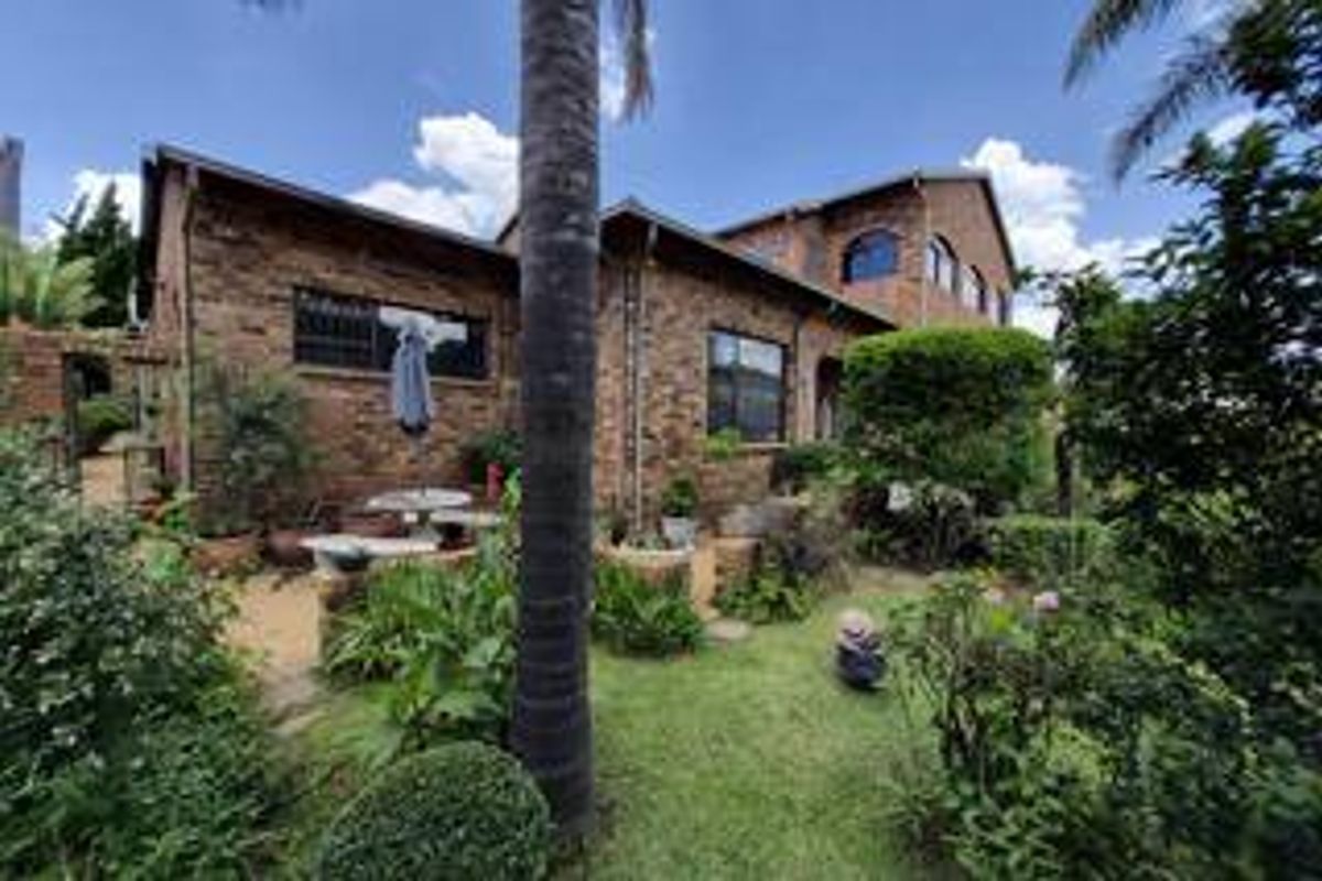 A rear view of a face-brick house featuring an arched window, a paved patio area, and a well-established garden.