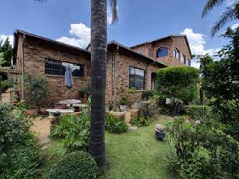 A rear view of a face-brick house featuring an arched window, a paved patio area, and a well-established garden.