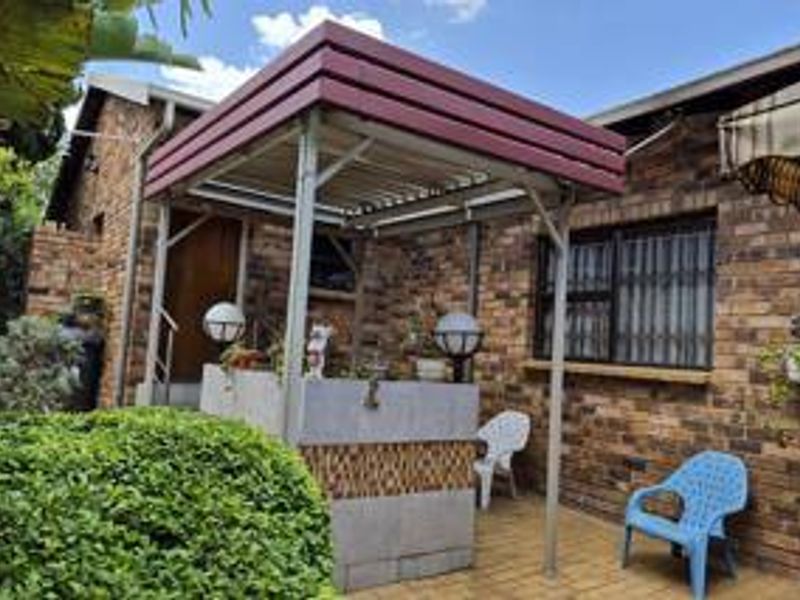 Outdoor patio area featuring a brick facade, paved flooring, and a built-in braai station under a metal pergola structure.