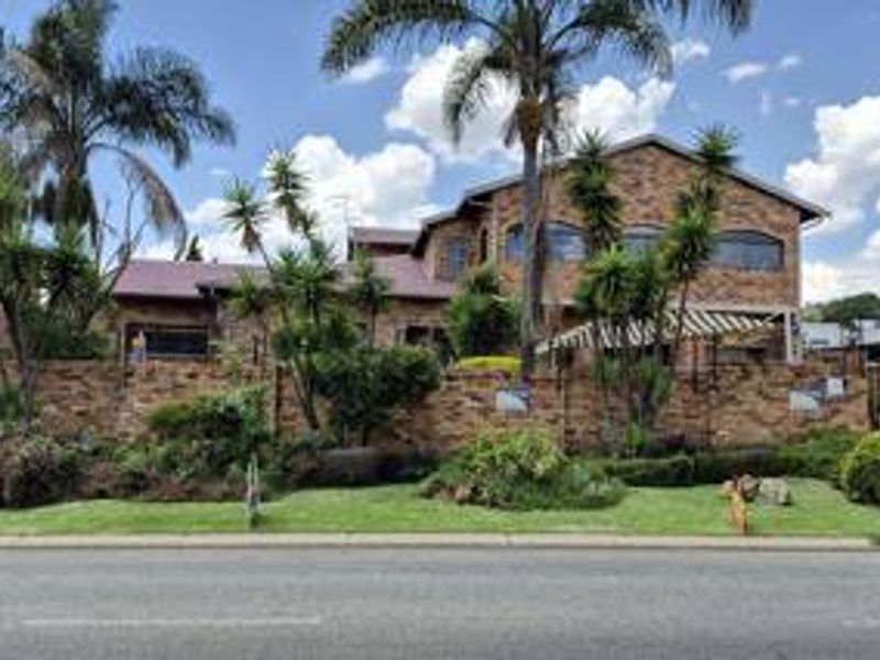A well-maintained double-story face brick house featuring arched windows, a tiled roof, and an established front garden with a secure boundary wall.