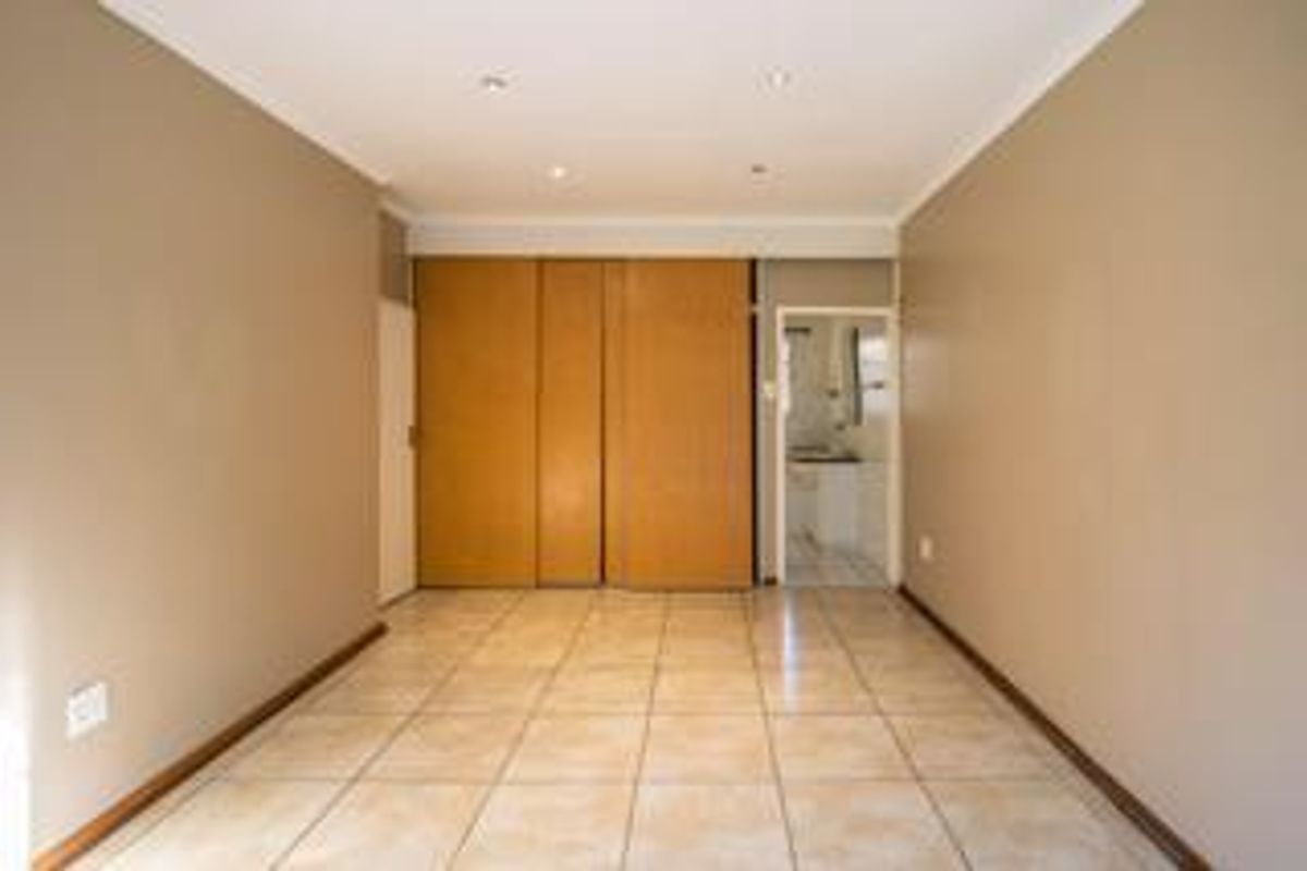 An empty bedroom featuring tiled flooring, built-in wooden cupboards, and recessed downlighting, offering a clean and neutral space ready for personalization.