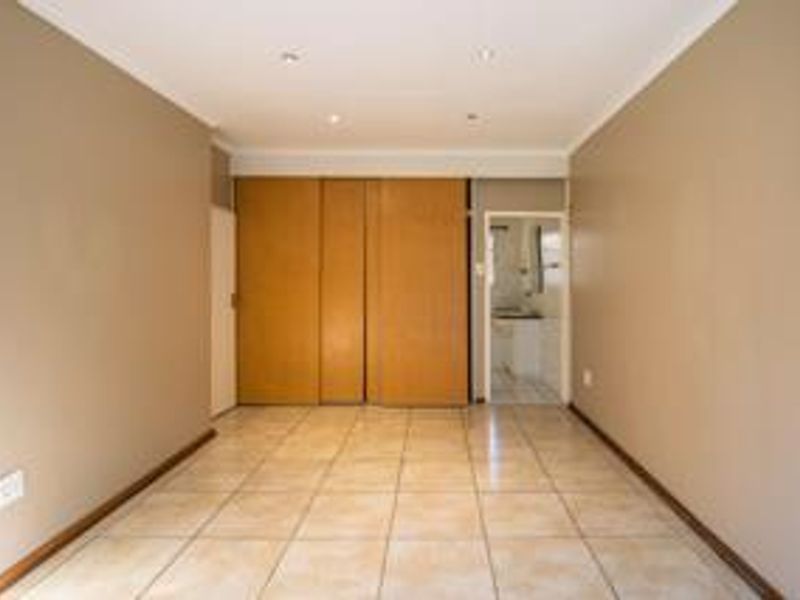 An empty bedroom featuring tiled flooring, built-in wooden cupboards, and recessed downlighting, offering a clean and neutral space ready for personalization.