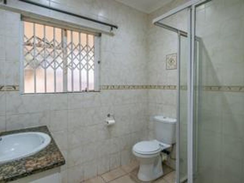 A functional bathroom featuring a shower enclosure, toilet, and vanity basin with a granite countertop, finished with neutral wall tiles.