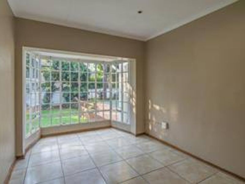 A bright, empty living room featuring large bay windows with garden views and neutral tiled flooring.