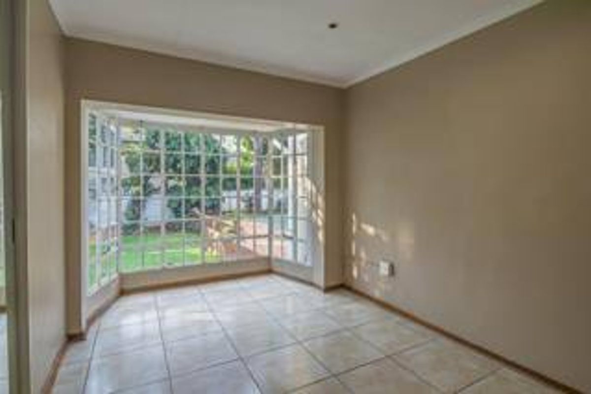 A bright, empty living room featuring large bay windows with garden views and neutral tiled flooring.