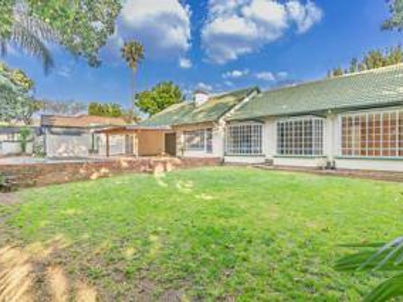Rear view of the house featuring a spacious lawn, covered patio area, and multiple bay windows under a tiled roof.