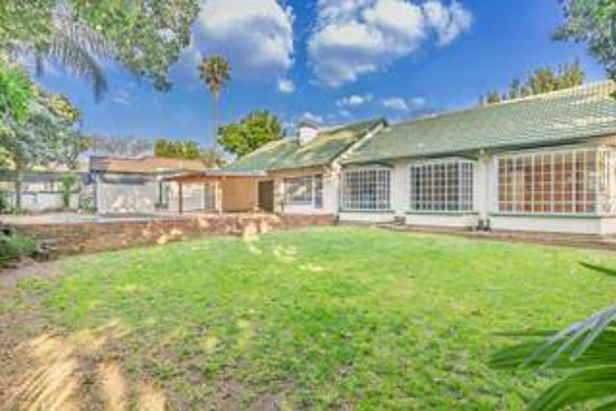 Rear view of the house featuring a spacious lawn, covered patio area, and multiple bay windows under a tiled roof.
