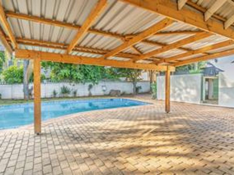 Outdoor entertainment area featuring a swimming pool, paved patio, and a covered timber pergola structure.