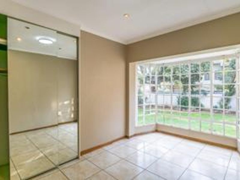 Bright bedroom featuring large bay windows, tiled flooring, and a spacious built-in mirrored wardrobe.