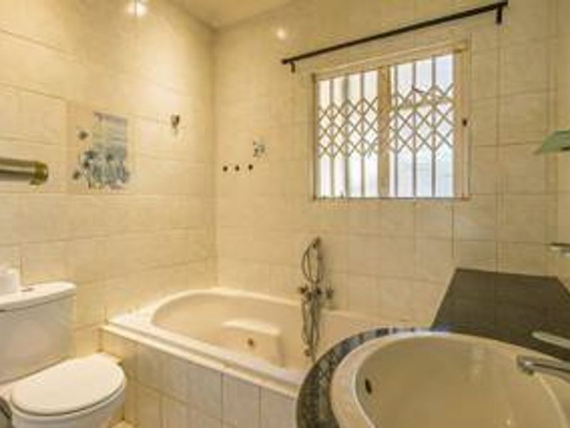 A functional bathroom featuring a built-in bathtub, vanity basin, toilet, and tiled walls with security bars on the window.