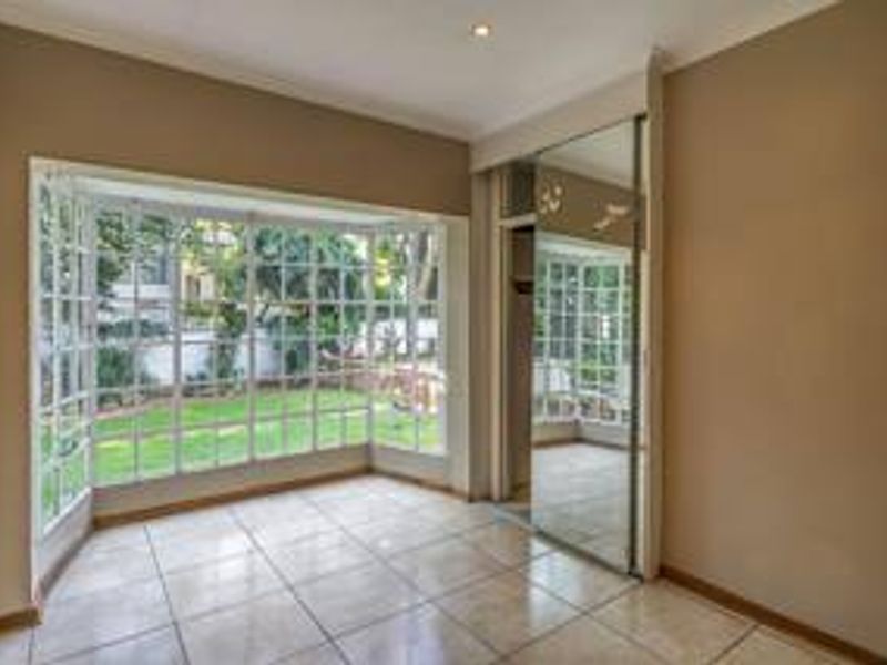 A bright, empty bedroom featuring large bay windows, tiled flooring, and mirrored built-in cupboards, offering a clean and versatile space.