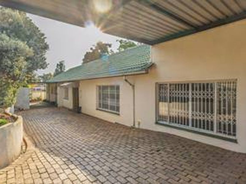 Front exterior view of the property featuring a paved driveway, covered carport, and secure window treatments.