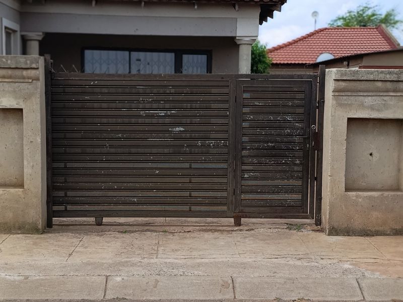 Front view of the property featuring a metal sliding gate, concrete boundary wall, and tiled roof structure.