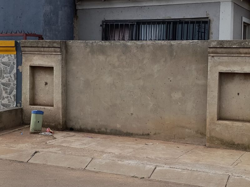 Street view of the property showing a concrete boundary wall, tiled roof structure, and security features from the roadside.