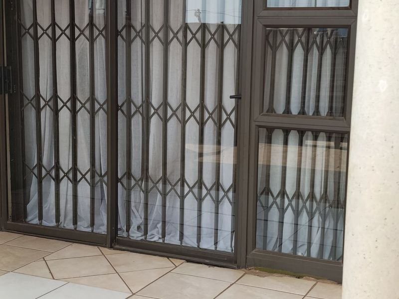 A covered patio area featuring tiled flooring, a structural concrete pillar, and sliding glass doors secured with metal security gates.