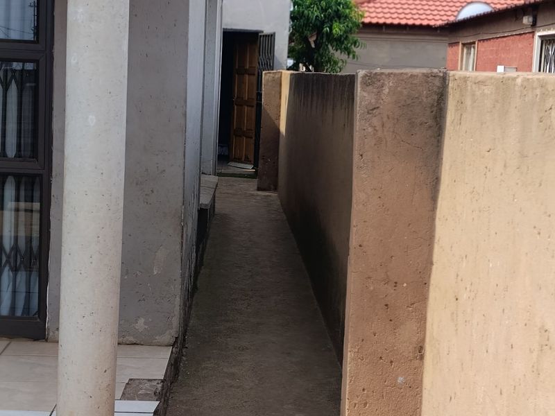 A narrow side passage between the house and the boundary wall, featuring a concrete pathway and a structural support column.
