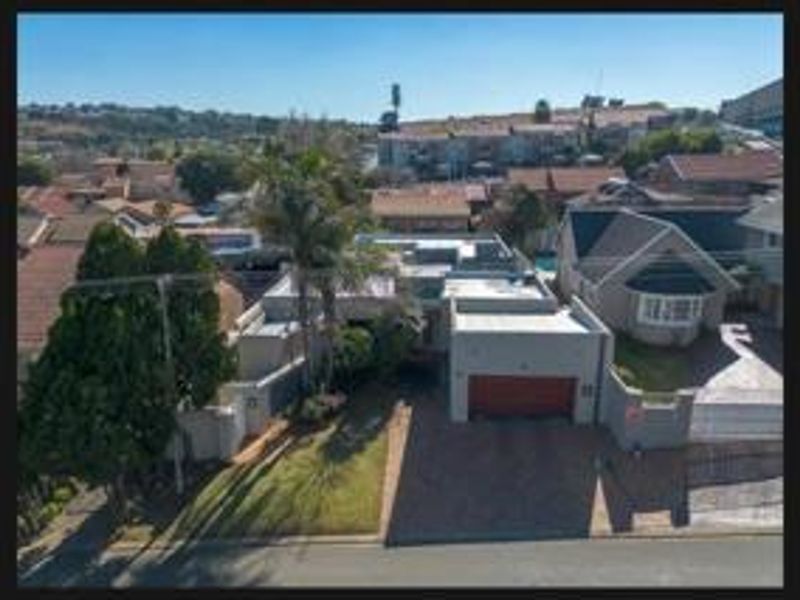 Aerial view of the property showing the front facade, paved driveway, garage, and surrounding residential neighborhood.