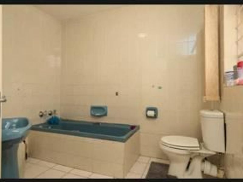 A dated bathroom featuring a built-in bathtub, pedestal basin, and toilet with neutral wall tiling.