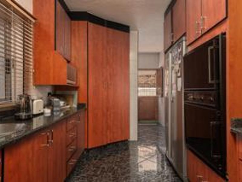 A functional kitchen featuring warm-toned wooden cabinetry, granite countertops, integrated oven, and built-in microwave with polished tiled flooring.