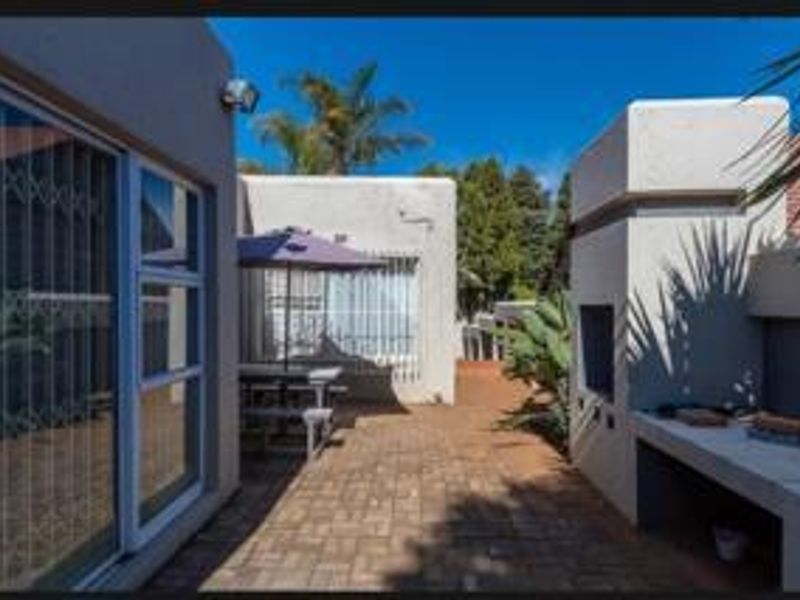 Outdoor patio area featuring a built-in braai, paved flooring, and direct access to the home through sliding doors with security gates.
