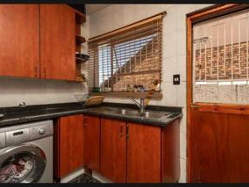 A functional laundry room featuring built-in wooden cabinetry, granite countertops, a stainless steel sink, and direct access to the exterior.