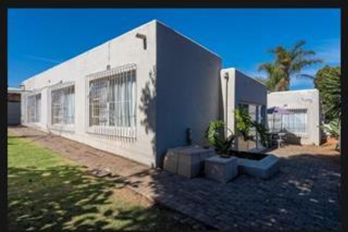 Rear exterior view of the house featuring a paved patio area, lawn, and security bars on the windows.